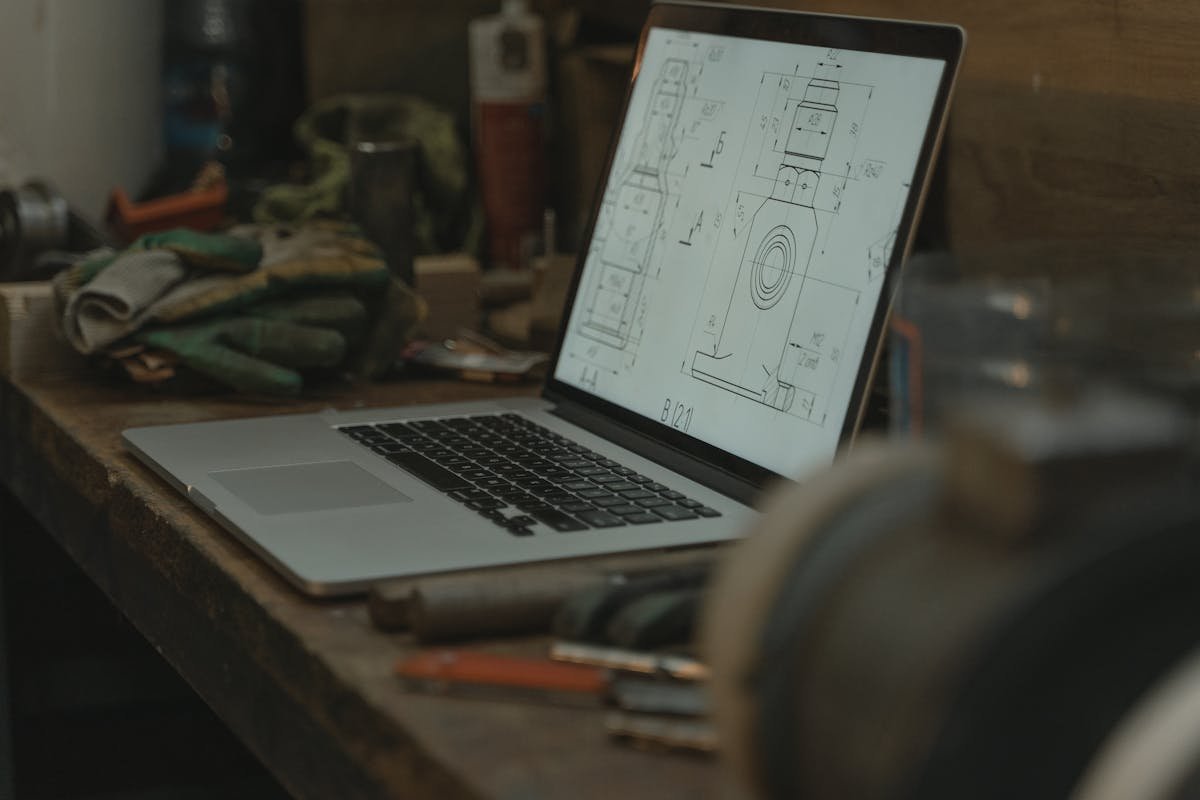 Laptop displaying engineering drawings with rolled paper blueprints — common CAD design mistakes